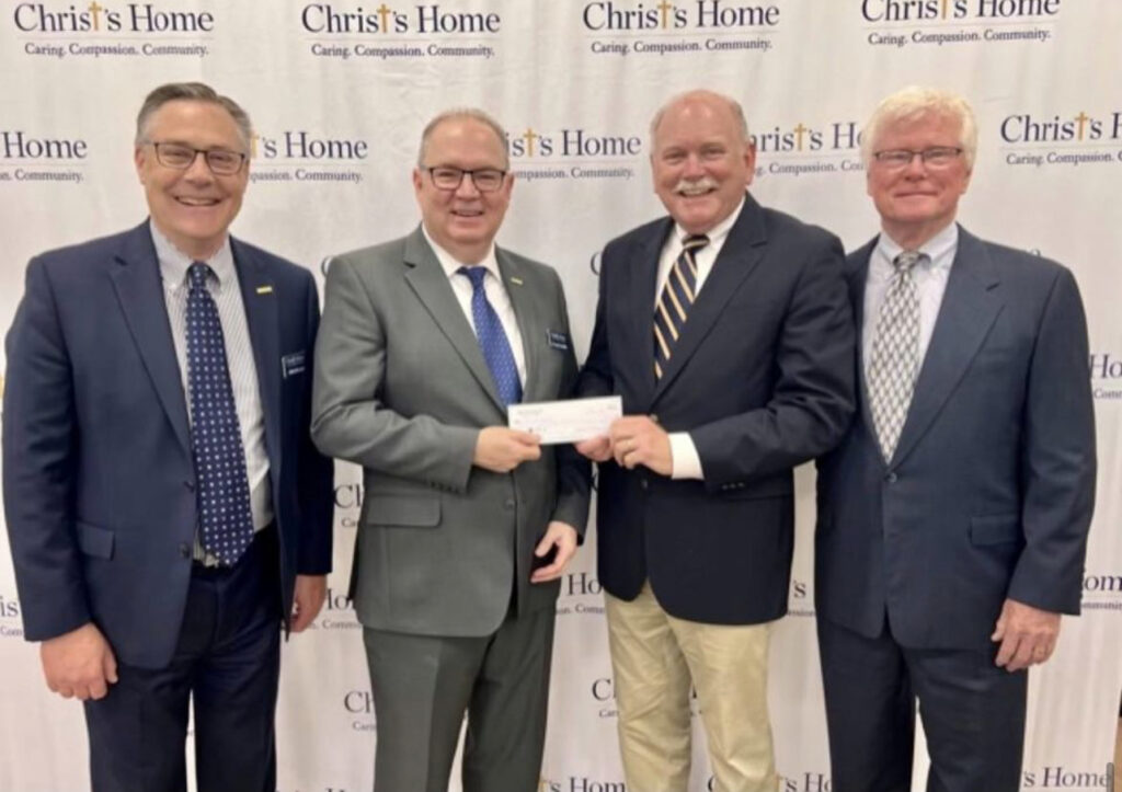 Four men in suits and ties holding a check.